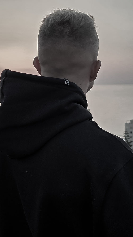 Back view of a man wearing the black Konna sustainable minimal hoodie, looking out over the water.
