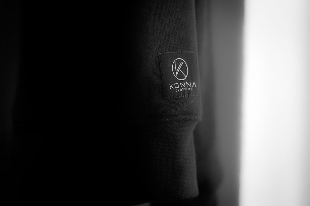 Close-up detail shot of the Konna Clothing brand patch of a black premium hoodie.